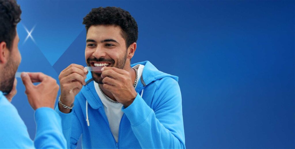 Man using Guru Nanda Premium Whitening Strips while smiling, showing teeth whitening strip application with a bright and confident smile.